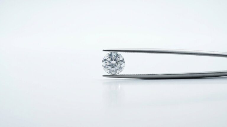 A round brilliant lab grown diamond held in jeweller's tweezers against a white background.